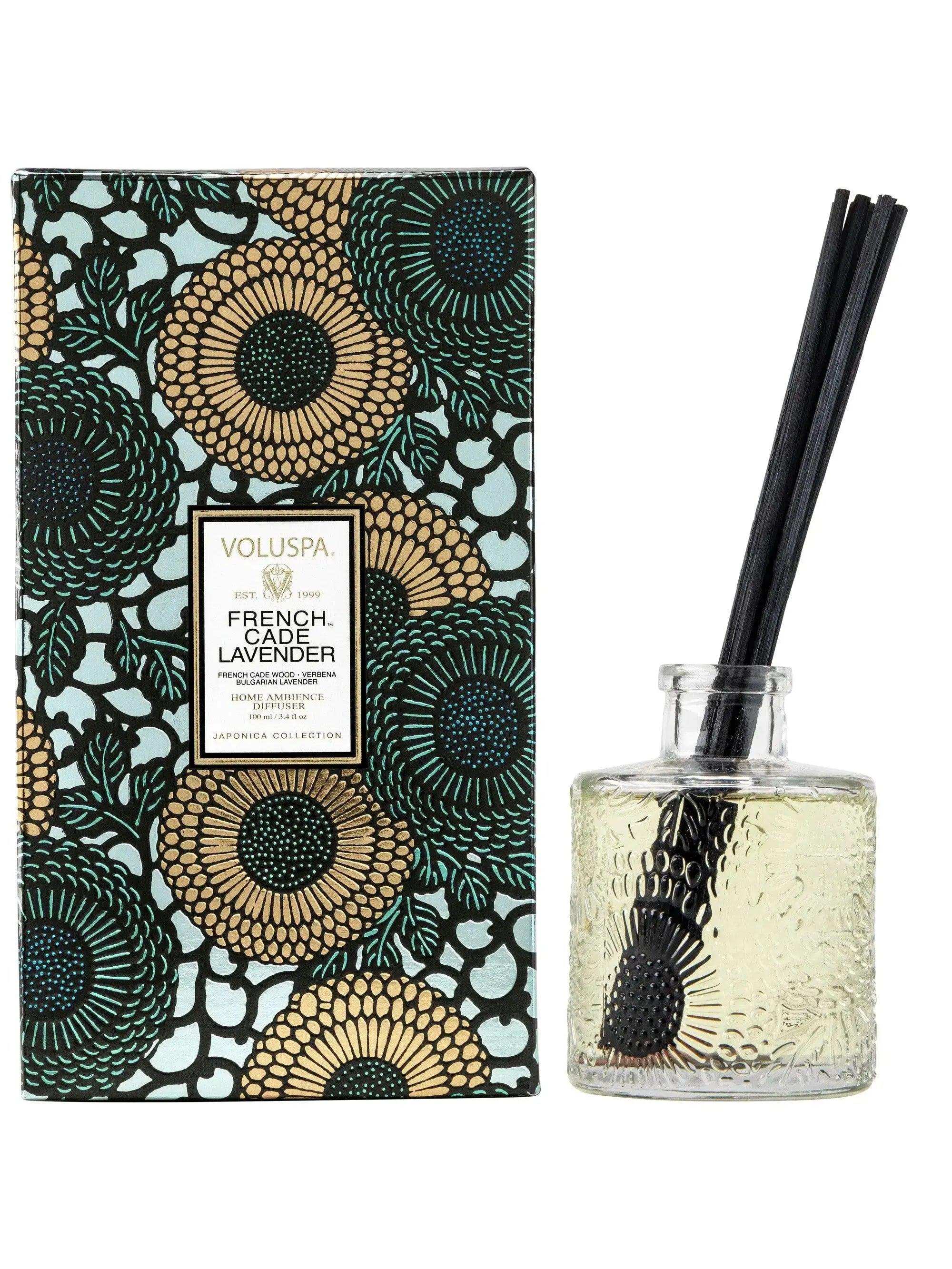 Voluspa French Cade Lavender Reed Diffuser, glass vessel with black reeds beside a green and gold patterned box