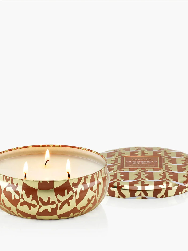 Voluspa Gingerbread Chalet 3-Wick Tin Candle, three lit wicks in a brown and cream tin with the lid beside it